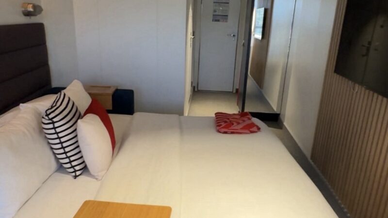 Virgin Voyages cruise ship cabin with white bedding and wall TV