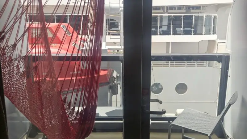 Cabin balcony on a Virgin Voyages cruise ship with a red hammock and chair