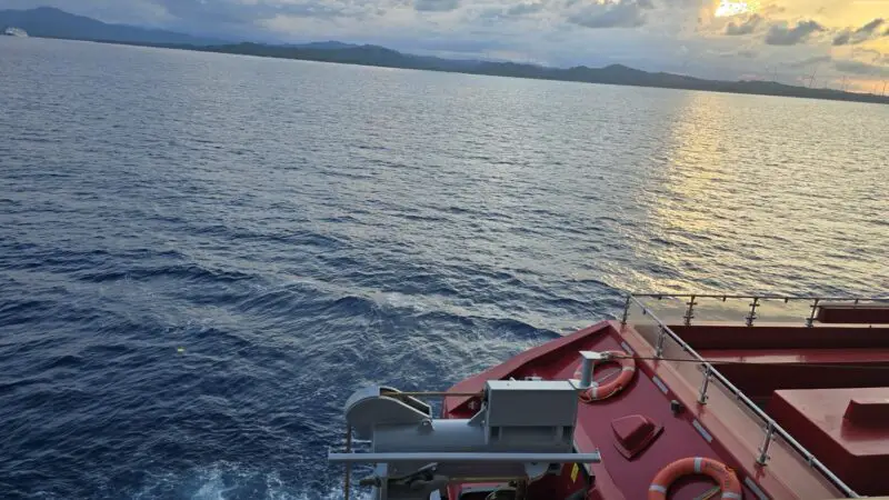 Sunset over the ocean from a ship deck with red railings and lifebuoys