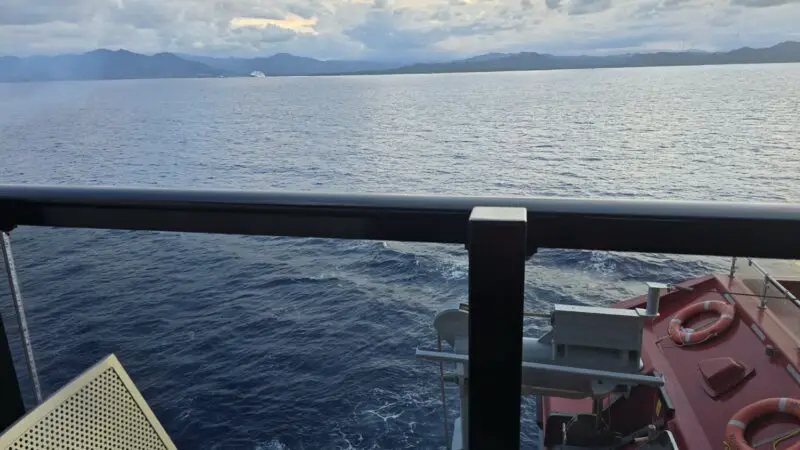 View of the ocean from a ship deck with a railing and lifeboat on the right