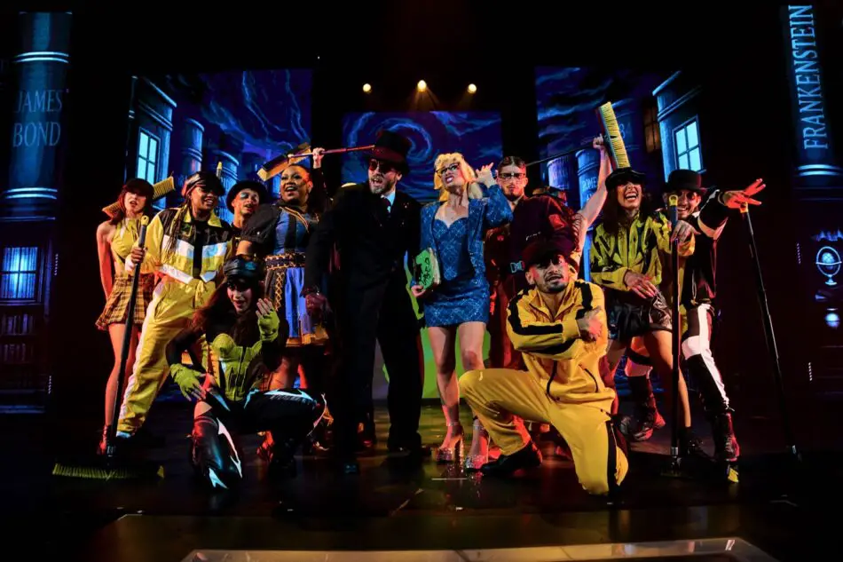 Group of performers on a colorful stage wearing 1960s-inspired costumes under bright lighting