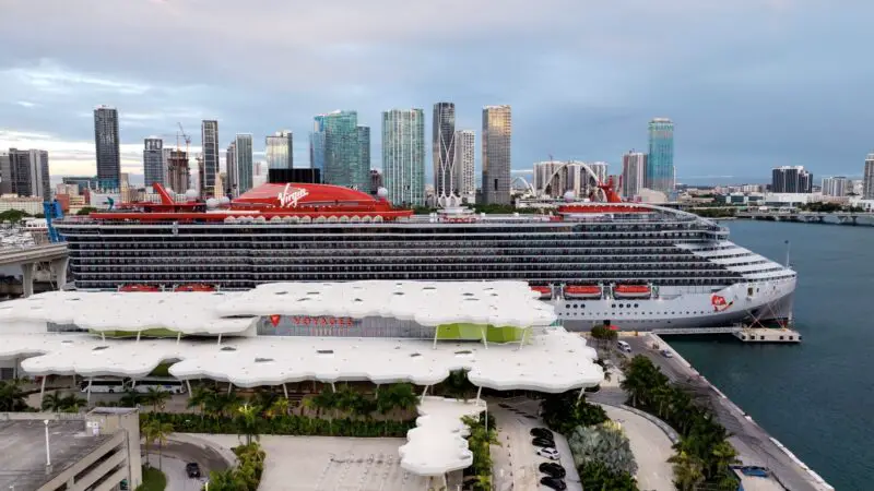 Virgin Voyages cruise ship docked at port with city skyline