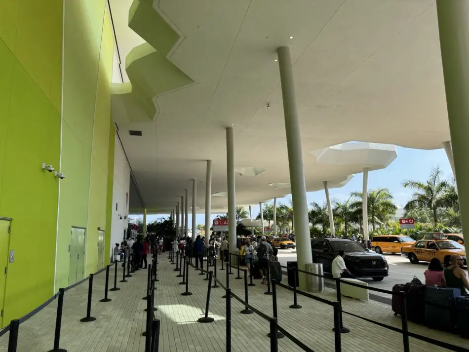 Passengers queue with luggage outside a lime green terminal under a white canopy