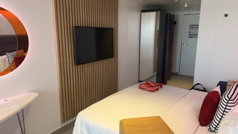 Virgin Voyages cruise ship cabin with bed wall TV and round orange mirror
