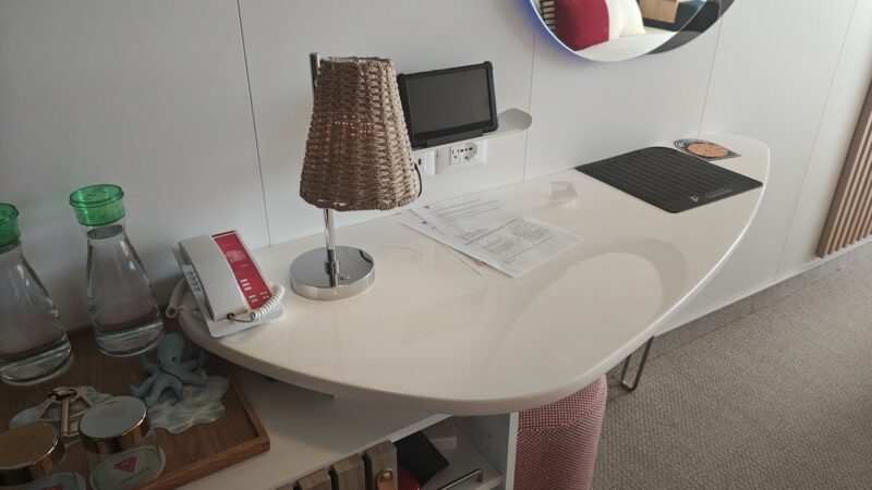 Cruise cabin desk area on a Virgin Voyages ship with lamp and mirror