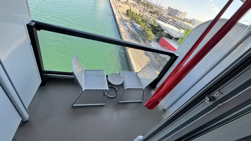 Balcony with two white chairs and a small table on a Virgin Voyages cruise ship overlooking the harbor
