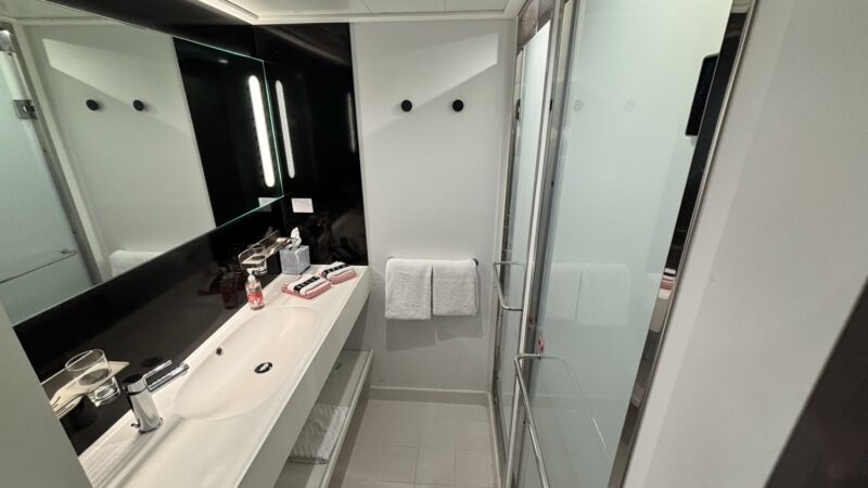 Modern cruise ship bathroom with sink, towels, and glass shower on a Virgin Voyages ship