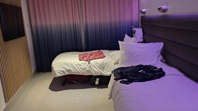 Twin beds in a Virgin Voyages cabin with purple ambient lighting