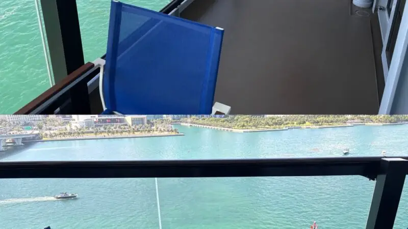 Balcony on a Virgin Voyages cruise ship with blue chairs and a red hammock overlooking turquoise water and city skyline