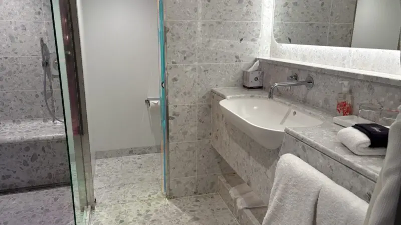 Shipboard bathroom with glass shower and sink on a Virgin Voyages cruise shi