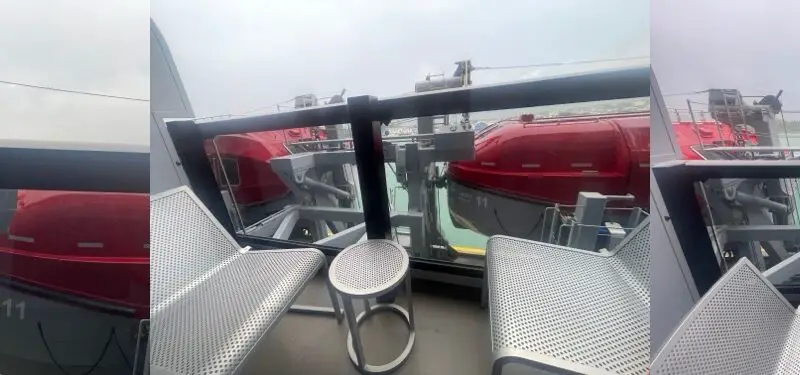 Balcony on a Virgin Voyages cruise ship with metal chairs and a round table, lifeboats visible
