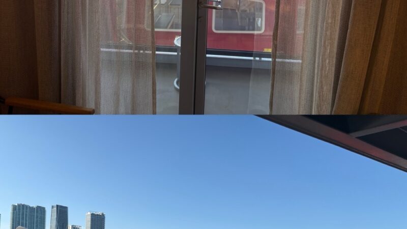 Inside a Virgin Voyages cabin with balcony doors looking out at a red ship and city skyline