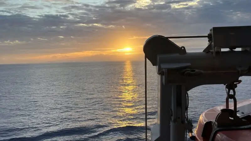 Sunset over the ocean from a Virgin Voyages cruise ship deck with lifeboats and equipment