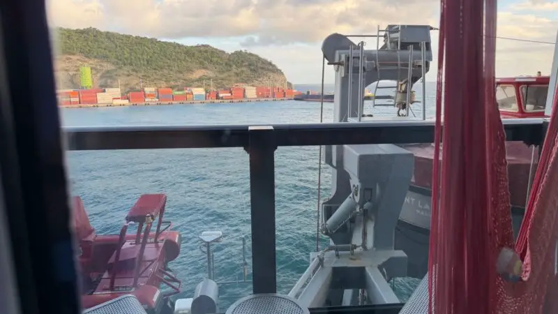 View from a Virgin Voyages cabin window overlooking a container port and sea