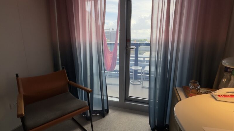 A Virgin Voyages cruise ship cabin with pink to blue curtains and balcony view