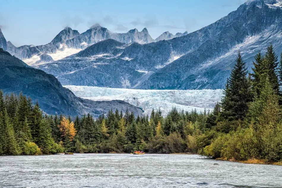 Glacier valley with a wide river, evergreen forest, and distant snow-capped mountains