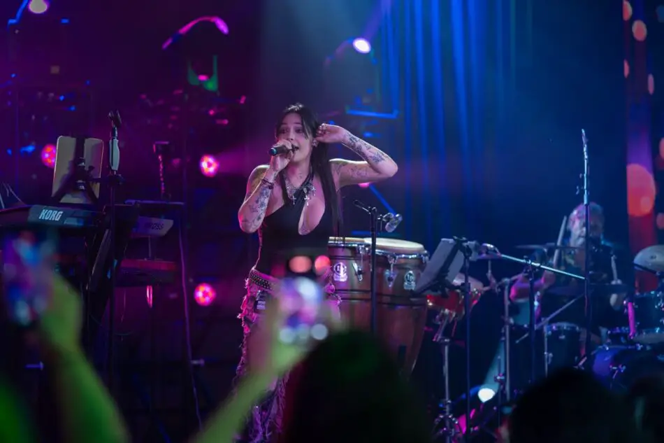 Tattooed female singer performs on a concert stage with a live band under colorful lights