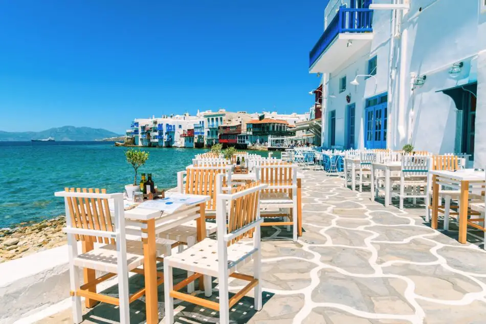 Outdoor seaside cafe with white and wood tables on a Greek island