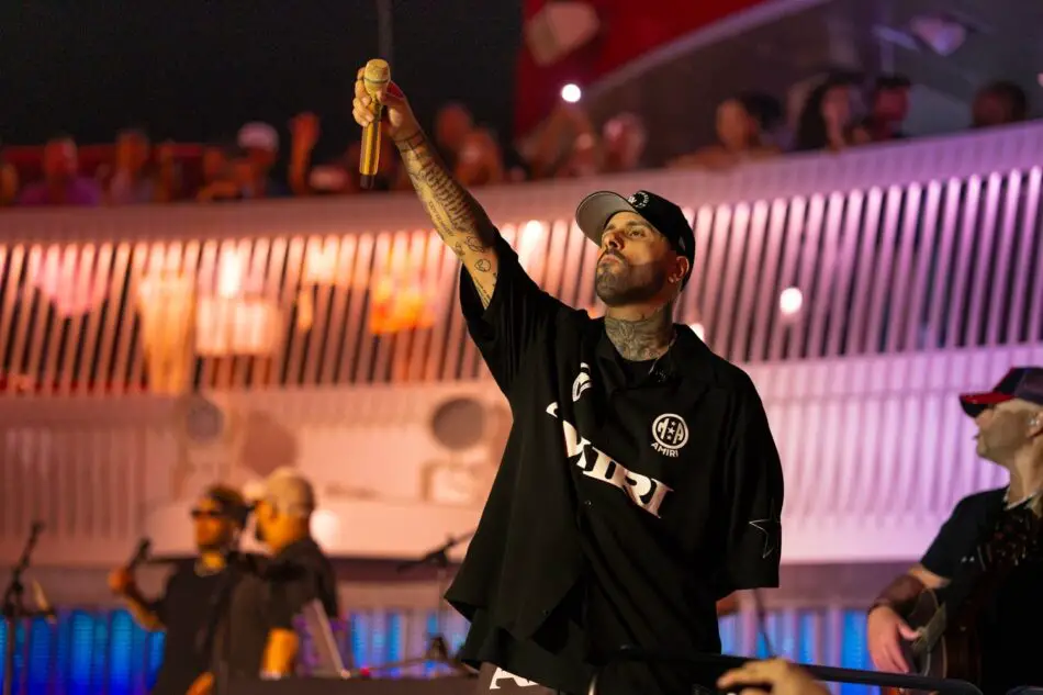 Tattooed male singer raises a microphone on stage during a concert with an audience in the background