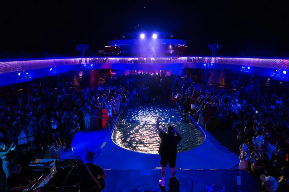 Crowd gathered around a lit pool on a Virgin Voyages cruise ship at night