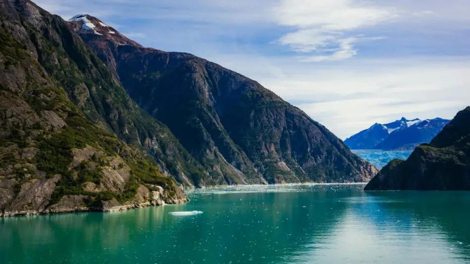 A serene turquoise lake surrounded by towering green mountains under a partly cloudy sky.