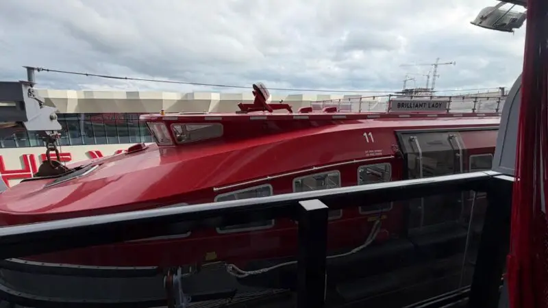 Inside a Virgin Voyages cabin overlooking a red lifeboat on the deck