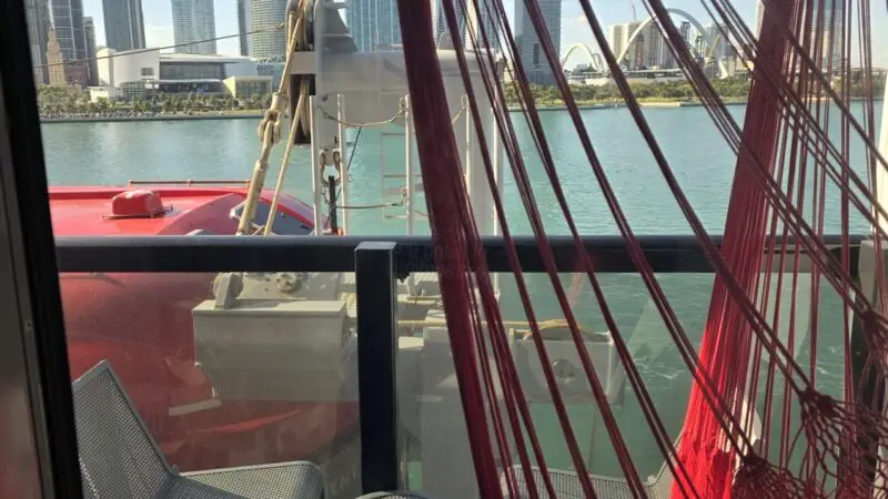 Balcony seating with a red hammock on a Virgin Voyages cruise ship overlooking the city skyline