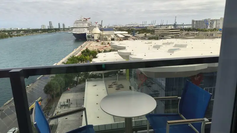 Balcony with blue chairs and round table on a Virgin Voyages cruise ship overlooking a port