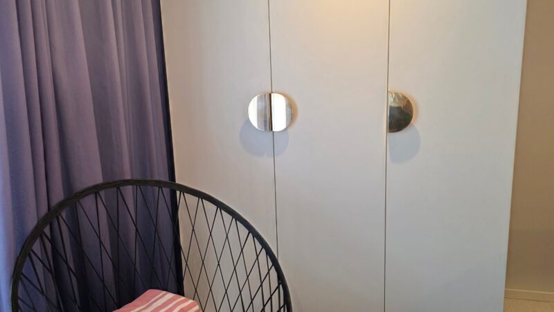 Virgin Voyages cruise ship cabin interior with a modern chair holding folded pink-striped towels, next to a wall with circular handles and purple curtains.