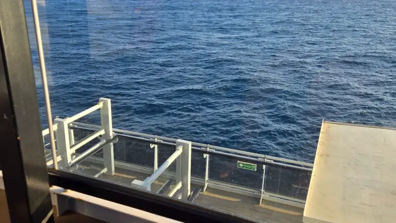 View from a Virgin Voyages cruise ship balcony overlooking the ocean, with a barrier and sea in the background.