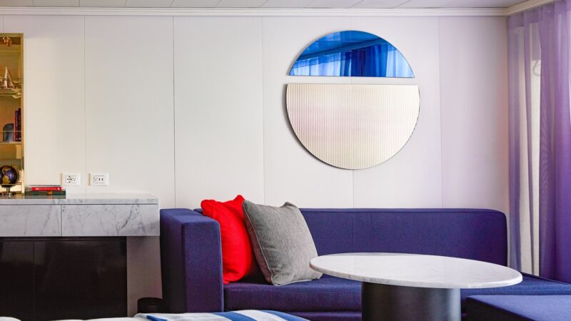 Cozy hotel style seating area with purple sofa, red and gray cushions, marble table on a Virgin Voyages cruise ship