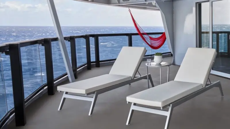 Two white lounge chairs on a Virgin Voyages cruise ship balcony with an ocean view and a small table