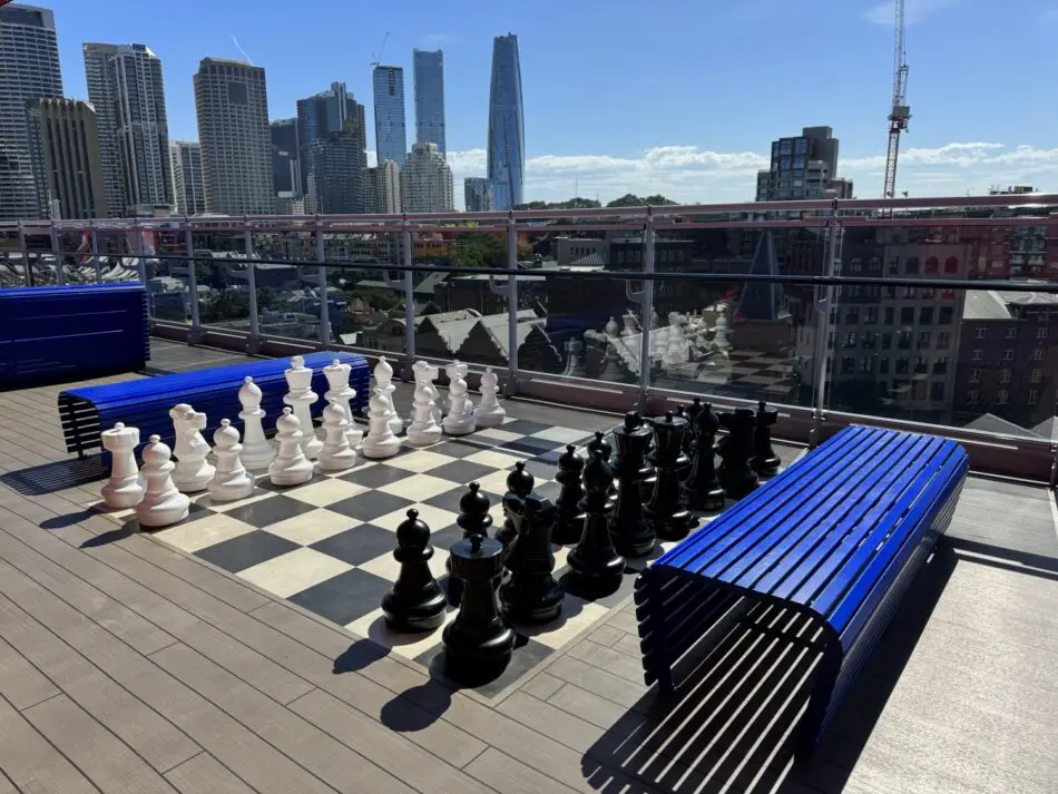 Rooftop terrace with a large outdoor chessboard and blue benches against a city skyline