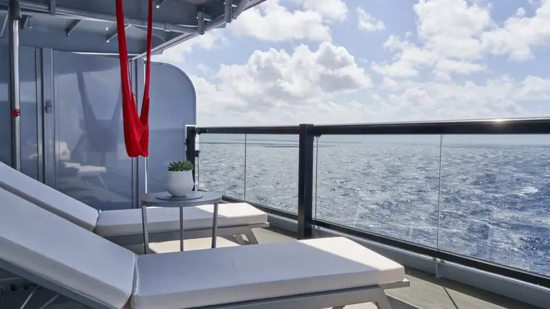 Balcony on a Virgin Voyages cruise ship with white lounge chairs overlooking the sea