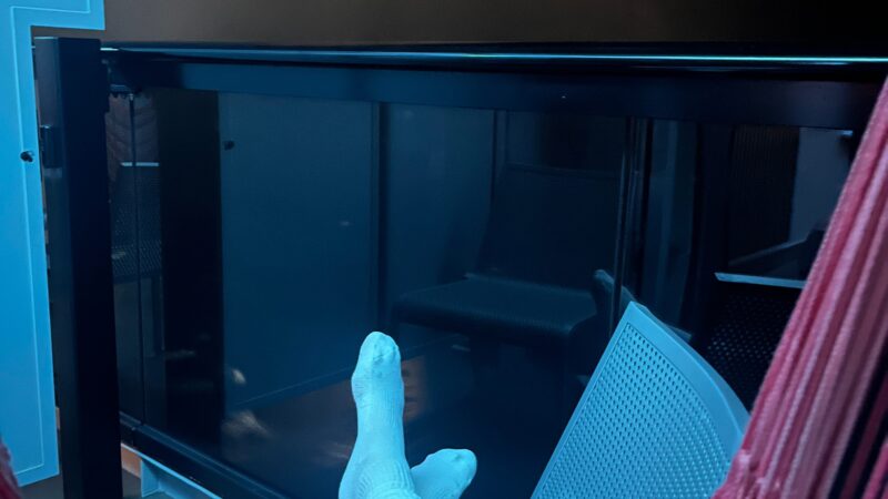 View of a Virgin Voyages cruise ship balcony cabin at night, featuring a person relaxing in a hammock with a pair of headphones resting on their lap.