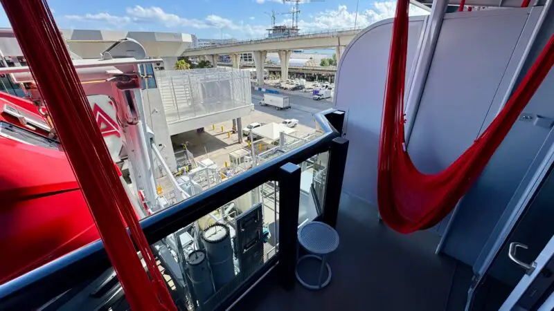 Virgin Voyages cruise ship balcony with a red hammock, small table, and view of the port.