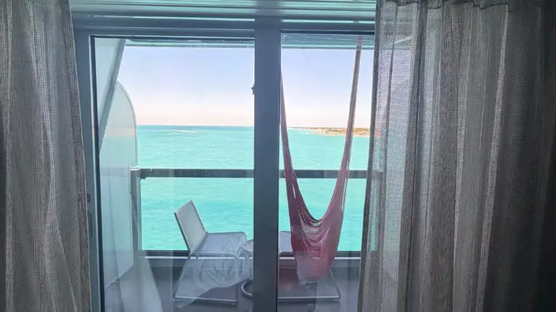 Virgin Voyages cruise ship cabin with a balcony view showing chairs and a hammock overlooking the ocean.