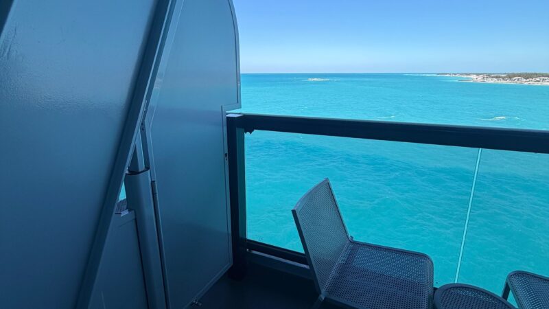 Cruise ship balcony with a chair and small table overlooking the ocean.