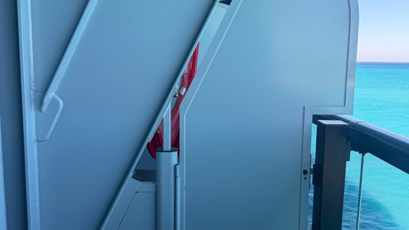 Virgin Voyages cruise ship balcony with safety railing, metal partition, and ocean view.