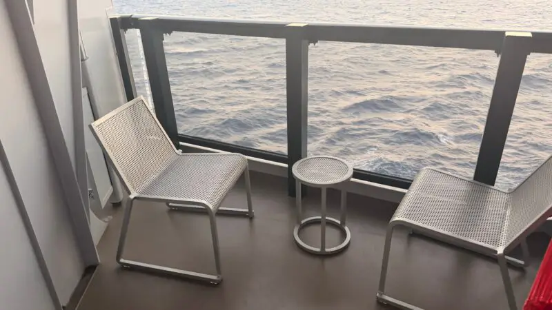 Balcony of a Virgin Voyages cruise ship cabin with two chairs and a small table overlooking the ocean.