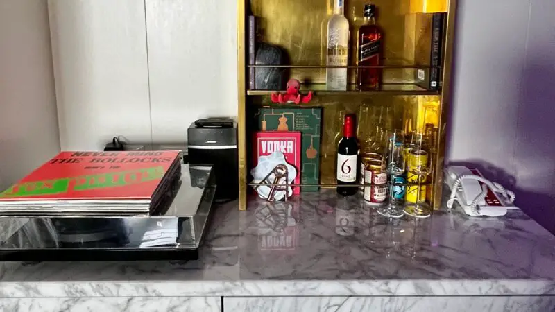 A marble countertop with a turntable and record, and a shelf stocked with various liquor bottles and glasses.