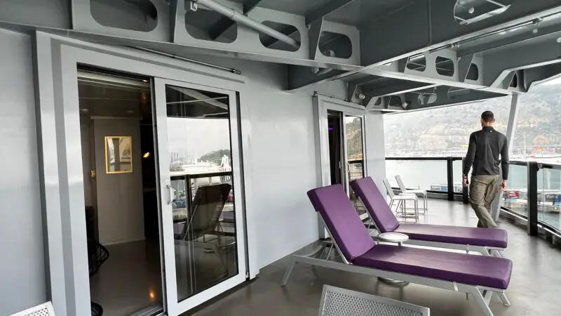 Virgin Voyages cruise ship balcony with sliding glass doors, purple lounge chairs.