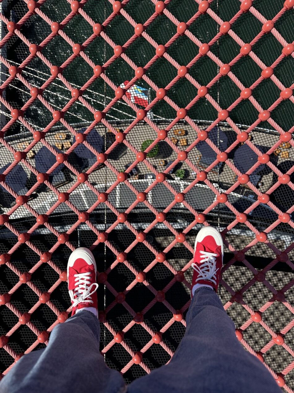 Person in red sneakers stands on red rope netting above a deck