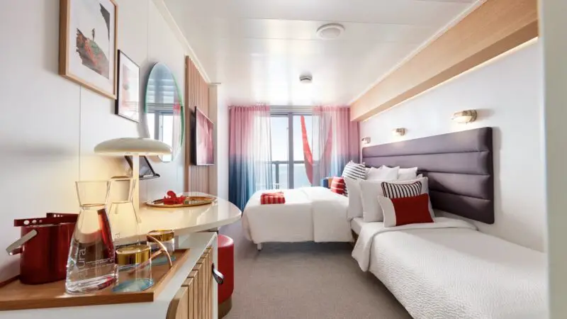 Twin beds in a bright Virgin Voyages cruise ship cabin with a sea view