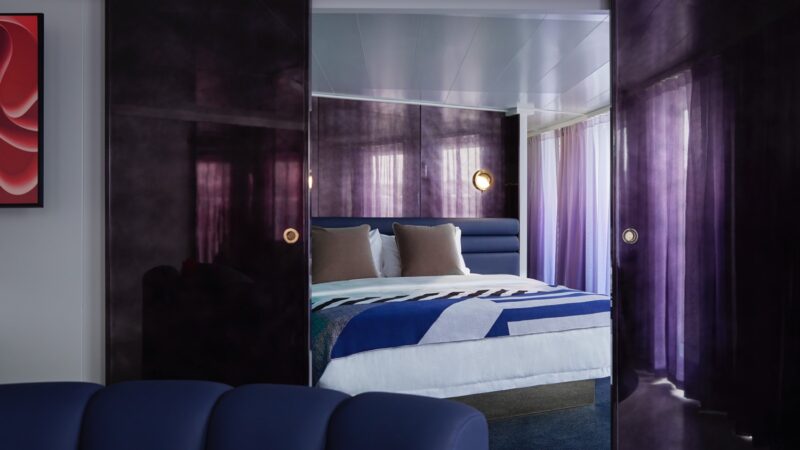 Luxurious cruise cabin on a Virgin Voyages cruise ship with purple walls and blue upholstered bed
