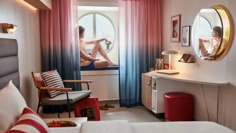 Virgin Voyages cabin on a cruise ship with circular window and pink to blue curtains