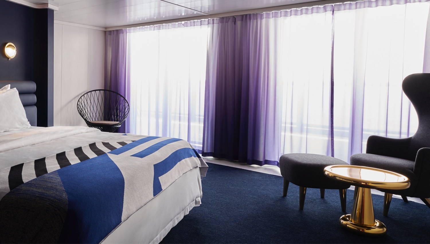 Virgin Voyages cruise ship cabin with bed, lounge chair, and purple curtains