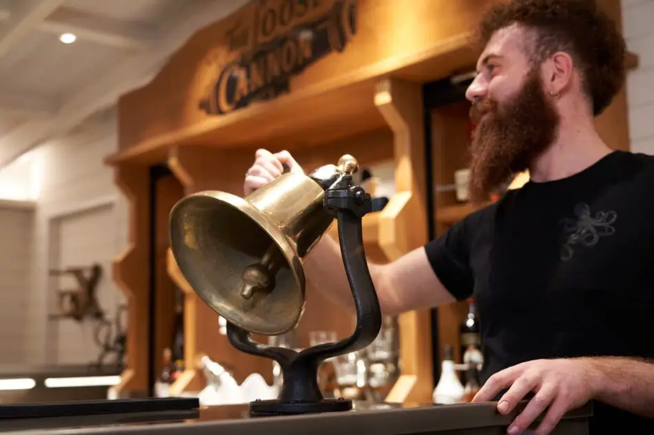 Bearded man behind a bar uses brass ship's speaking trumpet