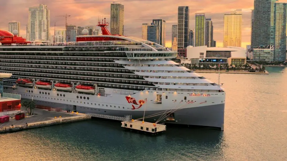 Scarlet Lady, a Virgin Voyages cruise ship, docked by city skyline