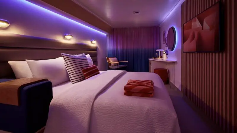 Virgin Voyages cabin on a cruise ship with a large bed and purple mood lighting